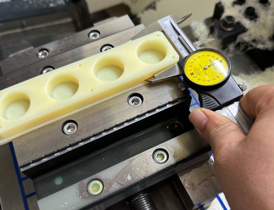 In-process quality inspection of a CNC machined plastic part using a Mitutoyo dial caliper on a machine tool vise.